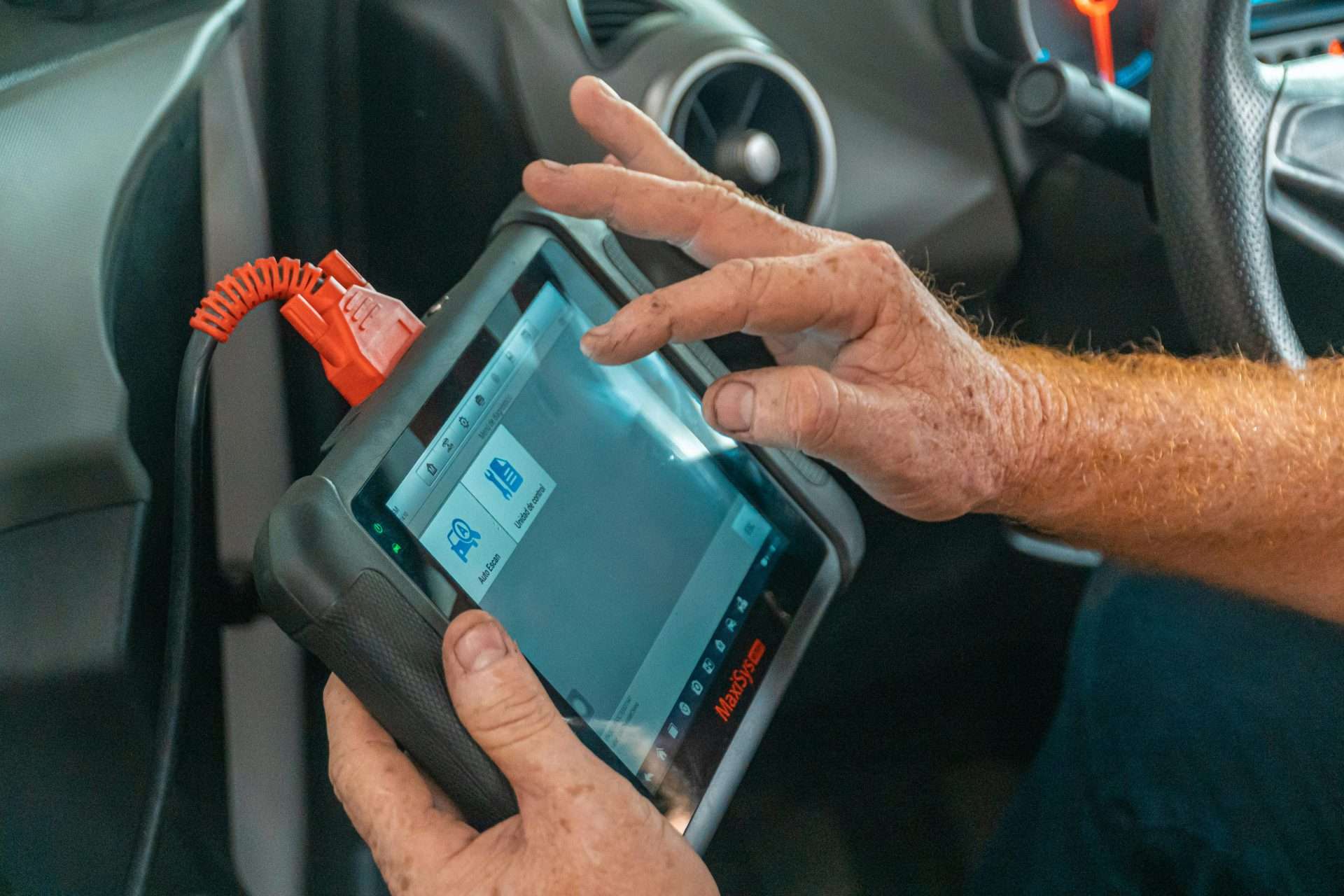 Mécanicien utilisant un outil de diagnostic à l'intérieur d'une voiture pour vérifier les problèmes de moteur et assurer un entretien approprié.